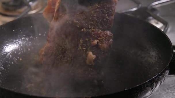 一片牛肉牛排 配上调味品 黄油和大蒜 慢动作放在锅里煎 厨房的钳子会变成一块肉 — 图库视频影像