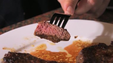 Tabakta büyük bir parça taze ızgara biftek. Ağır çekimde kanla birlikte orta pişmiş et. Bir çatal ve bıçak yakın görüntü kesiyor.