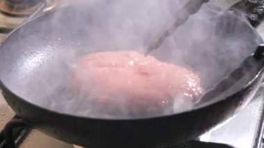 Bir parça çiğ et yavaş çekimde tavada kızarır. Kızarmış et çatırdıyor ve sigara içiyor..