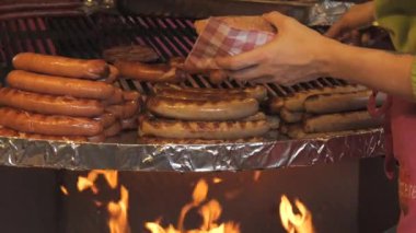 Sosislerin kızartıldığı ve satıcıların satıldığı büyük yuvarlak bir ızgara. Büyük bir ateş alevi et ürünlerini yavaş çekimde bir gıda pazarında kızartıyor..