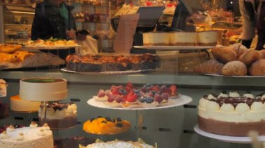 Dükkanın tezgahında bir sürü farklı lezzetli taze kek vardı. İnsanlar geçiyordu. Pencerenin camına yansıyordu..