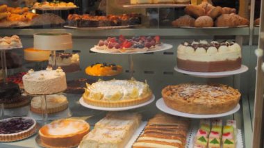 Baden-Baden, Almanya - 17 Aralık 2023: Bir tezgahın üstünde bir çok farklı lezzetli taze meyve ve meyveli kek, insanlar geçiyor, vitrinin camına yansıyor
