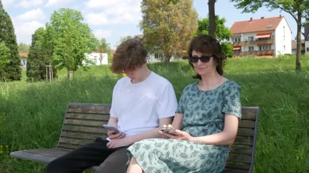 어머니와 아들은 공원에서 벤치에 스마트 폰을보고 화면을 누르고 자신의 전화를 — 비디오