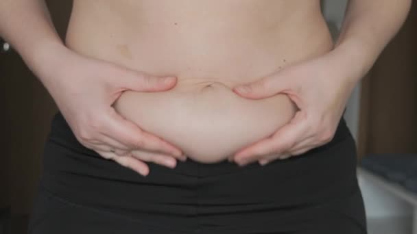 女性の腹の体は陽性です 女性は平らに腹の折り畳みに触れる スポーツブラとレギンスを身に着けている女性の腹部に脂肪の小さな層 スポーツ 健康的なライフスタイル または太りすぎのコンセプト — ストック動画