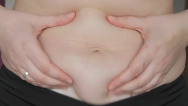 女性の腹の体は陽性です 女性は平らなゆっくりとした動きで腹の折り畳みに触れます スポーツブラとレギンスを身に着けている女性の腹部に脂肪の小さな層 スポーツ 健康的なライフスタイル または太りすぎのコンセプト — ストック動画