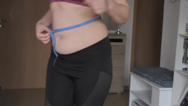 女性腹部身体呈阳性 一个女人测量她的腰围 女性穿着运动胸罩和腿的腹部有一层脂肪 健康生活方式或超重的概念 — 图库视频影像