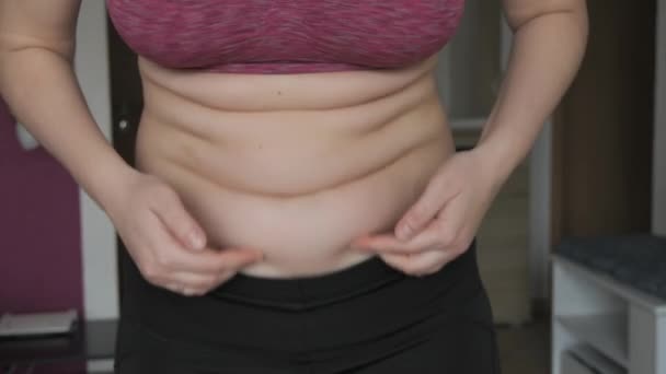 女性腹部身体呈阳性 女人以平缓的慢动作触摸腹部褶皱 身穿运动胸罩和腿的妇女腹部的一层脂肪 健康生活方式或超重的概念 — 图库视频影像