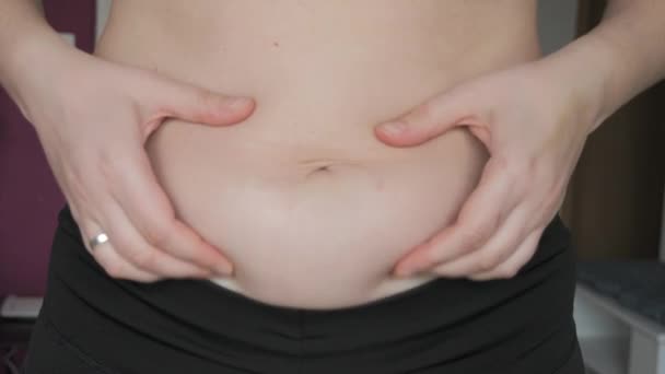 女性の腹の体は陽性です 女性は平らなゆっくりとした動きで腹の折り畳みに触れます スポーツブラとレギンスを身に着けている女性の腹部に脂肪の小さな層 スポーツ 健康的なライフスタイル または太りすぎのコンセプト — ストック動画