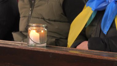Büyük beyaz bir mum, mavi ve sarı Ukrayna bayrağının arkasındaki bir kilisede cam bir şamdan kavanozunda yanar..