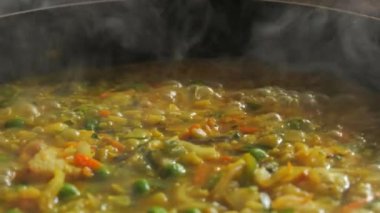Büyük bir tava köpüklü risotto kaynıyor. Ev mutfağında sebzeli ve tavuklu risotto hazır..