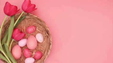 Paskalya Hareketi animasyonu. Çeşitli Paskalya yumurtaları pembe tonlarda pembe mercan arka planında hasır bir sepetin içinde güzel kırmızı lalelerin yanında hareket eder..