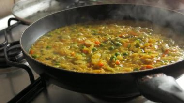 Büyük bir tava köpüklü risotto kaynıyor. Ev mutfağında sebzeli ve tavuklu risotto hazır..
