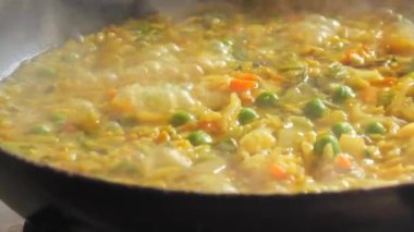 Büyük bir tava köpüklü risotto kaynıyor. Ev mutfağında sebzeli ve tavuklu risotto hazır..