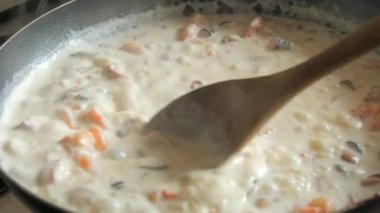 Ahşap bir mutfak kaşığı, tavada kızartılmış deniz ürünlerinde sıvı kremi karıştırır. Çeşitli midyeler, karidesler, ahtapotlar yakın çekim görüntüsünde yavaş kızartılır..