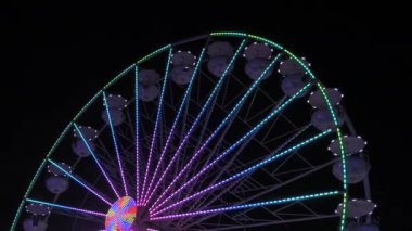 Geceleri dönme dolap. Çok renkli Aydınlatılmış tekerlek, tatilcileri beyaz kabinlerinde döndürür ve yuvarlar..