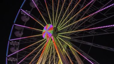 Geceleri dönme dolap. Çok renkli Aydınlatılmış tekerlek, tatilcileri beyaz kabinlerinde döndürür ve yuvarlar..
