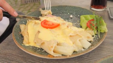 Restoranda bir ziyaretçi, restoranda çatal ve bıçakla kuşkonmazla yemek yer. Beyaz kuşkonmaz, krep, pastırma ve sos. Gurmeler için bahar yemeği.