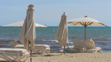 Güneş yatakları ve şemsiyeleri olan boş bir sahil. Ağır çekimde kirli dalgalarla fırtınalı deniz.