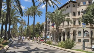 2 Temmuz 2024 - Palma de Mallorca, Mallorca: Palma şehrinde büyük mimari ve turistlerin bulunduğu rahat bir cadde. Güzel palmiye ağaçları