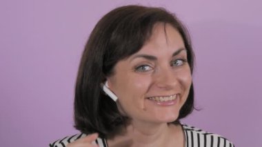 Kablosuz kulaklıkla müzik dinleyen, dans eden ve şarkı söyleyen neşeli genç bir kadının portresi. Mor arka planda bir kadının duyguları, ağır çekim..