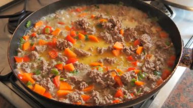 Yavaş çekimde sobanın üstünde tavayı yakın çekimde kaynayan bir et, doğranmış havuç, kırmızı ve yeşil dolma biberle birlikte haşlanarak zengin ve lezzetli bir karışım yaratıyor.