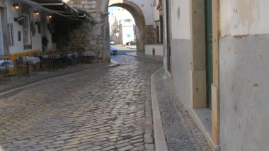 Estoi, Portekiz - 17 Ocak 2025 Faro Portekiz 'in tarihi merkezinde pitoresk bir kaldırım taşı caddesi. Dar virajlı yol geleneksel badanalı binalar ve rahat bir açık hava kahvesi ile kaplıydı.