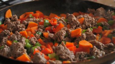 Yavaş çekimde sobanın üstünde tavayı yakın çekimde kaynayan bir et, doğranmış havuç, kırmızı ve yeşil dolma biberle birlikte haşlanarak zengin ve lezzetli bir karışım yaratıyor.
