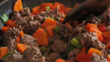 Ağır çekimde bir kadının elini ahşap bir kaşıkla karıştır et dolu bir tavayı karıştır kırmızı havuç ve yeşil dolma biber ve kaynayan et suyu kaynayan su ve buhar yükseliyor