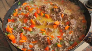 Yavaş çekimde sobanın üstünde tavayı yakın çekimde kaynayan bir et, doğranmış havuç, kırmızı ve yeşil dolma biberle birlikte haşlanarak zengin ve lezzetli bir karışım yaratıyor.