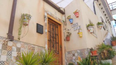 Alicante, İspanya - 22 Şubat 2025: Alicante, İspanya 'da büyüleyici tarihi bir mahalle olan Santa Cruz' un güzel bir manzarası. Resim, beyazlatılmış evleri olan geleneksel bir Akdeniz geçidini yakalıyor.