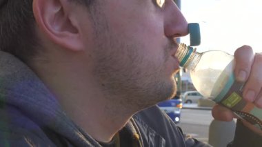 Plastik şişeden yavaş çekimde su içen bir adamın yakın çekimi. Güneş ışığı şişeden yansıyarak sıcak ve doğal bir parıltı yaratır. Sahne, susuzluğun önemini yakalar.