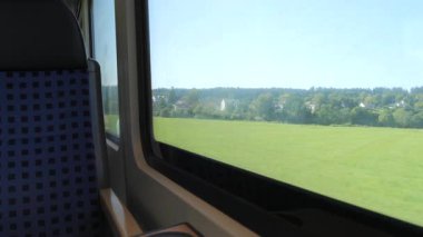 Mavi desenli koltukları ve tahta kollukları olan boş bir tren vagonunun huzurlu bir yavaş çekim görüntüsü. Geniş pencerelerden manzaralı bir kırsal alan yavaşça geçiyor ve rahatlatıcı bir manzara yaratıyor.