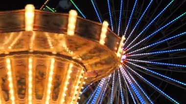 Geceleri parlayan dönme dolabın arka planına karşı ağır çekimde dönen güzel aydınlatılmış bir klasik salıncak. Dönme dolabın serin neon aksanıyla kontrastın sıcak altın ışıkları büyüleyici bir ışık yaratıyor.