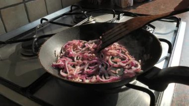 Gaz sobasında tavada sotelenen kırmızı soğanların yavaş çekim yakın çekimi. Buhar yavaşça yükselirken ahşap bir spatula soğanları karıştırır. Doğal ışık ve gerçekçi hareket sıcak, otantik bir ev yemeği atmosferi yaratır. Yemek için ideal.