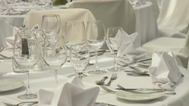 Güzel düzenlenmiş açık hava düğün masası. Taze çiçekler, zarif cam örtüler ve katlanmış peçeteler. Görüntü şenlikli ve romantik bir hava veriyor.