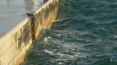 Deniz dalgalarının yakın çekim görüntüsü, altın saat boyunca modern bir taş gezinti alanına çarpıyor. Hırvatistan 'ın Zadar kentinde çekilen bu film, doğal okyanus hareketi ile temiz mimari çizgiler arasındaki zıtlığı vurguluyor. İlgili temalarda kullanım için ideal