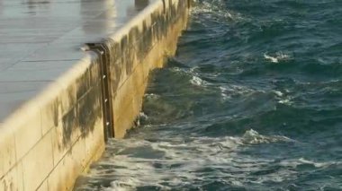 Deniz dalgalarının yakın çekim görüntüsü, altın saat boyunca modern bir taş gezinti alanına çarpıyor. Hırvatistan 'ın Zadar kentinde çekilen bu film, doğal okyanus hareketi ile temiz mimari çizgiler arasındaki zıtlığı vurguluyor. İlgili temalarda kullanım için ideal