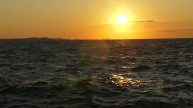 Adriyatik Denizi üzerinde, uzak Hırvat adalarının hafif dalgaları ve siluetleriyle batan altın güneşin göz kamaştırıcı manzarası. Seyahat, rahatlama veya doğa temalı içerik için ideal