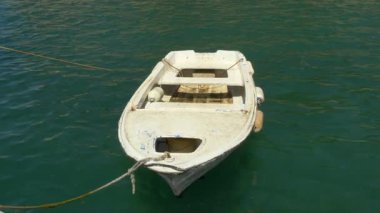 Yıpranmış beyaz bir kayık, sakin, zümrüt yeşili bir suda demirli. Teknede yaşlanma ve kullanım belirtileri var, kırsal cazibesini arttırıyor. Güneş ışığı dalgalanan yüzeyden yansıyor. Huzurlu bir deniz manzarasını çağrıştırıyor. Belki de sahilde sakin bir an.