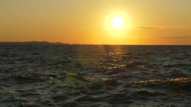 Hırvatistan 'ın Zadar kentinde çekilen Adriyatik Denizi üzerinde batan güneşin sinematik manzarası. Altın ışığın altında hafif okyanus dalgaları parıldıyor. Seyahat, hedef veya doğayla ilgili konular için ideal.