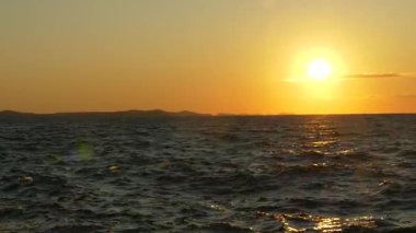 Hırvatistan 'ın Zadar kentinde çekilen Adriyatik Denizi üzerinde batan güneşin sinematik manzarası. Altın ışığın altında hafif okyanus dalgaları parıldıyor. Seyahat, hedef veya doğayla ilgili konular için ideal.