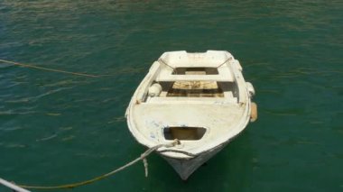 Yıpranmış beyaz bir kayık, sakin, zümrüt yeşili bir suda demirli. Teknede yaşlanma ve kullanım belirtileri var, kırsal cazibesini arttırıyor. Güneş ışığı dalgalanan yüzeyden yansıyor. Huzurlu bir deniz manzarasını çağrıştırıyor. Belki de sahilde sakin bir an.