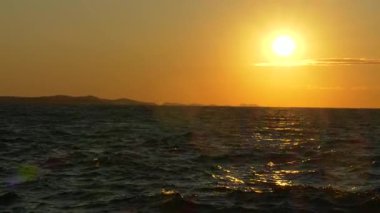 Sakin Adriyatik Denizi 'nin üzerinde, ılık ışığı yansıtan hafif dalgalarla batan güzel altın güneş. Hırvatistan 'ın Zadar kentinde yakalanan bu sakin deniz manzarası barışı, seyahat hayallerini ve ebedi güzelliği çağrıştırıyor