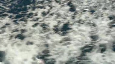 Derin mavi Adriyatik Denizi 'ndeki bir teknenin bıraktığı dinamik dalgalar ve köpüklü dalgaların yakın çekimi. Titreyen su yüzeyi dalgaların enerjisini ve ritmini yakalar.