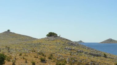 Parlak güneşli bir yamaçta sert beyaz kayalar ve yeşil bitki örtülerinin bir karışımı bulunur. Tepe bulutsuz bir gökyüzüne doğru yavaşça uzanıyor..