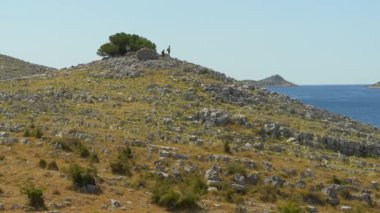 Parlak güneşli bir yamaçta sert beyaz kayalar ve yeşil bitki örtülerinin bir karışımı bulunur. Tepe bulutsuz bir gökyüzüne doğru yavaşça uzanıyor..