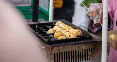 Bir adam takoyaki pişiriyor. Izgarada geleneksel yemek ve japan usulü ketçap. Yemek küçük ve yuvarlak, ve adam eldiven giyiyor.