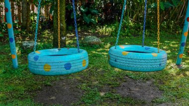 İki tekerlek salıncak maviye boyanmış sarı ve mavi noktalar çimenli bahçede zincirlerden sarkmış.