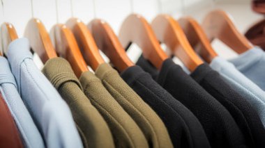 Renkli pamuklu takım elbiseler, korkuluktaki ahşap kumaş askısıyla asılır. Moda yaşam tarzı nesnesi, yakın plan ve seçici odaklanma.