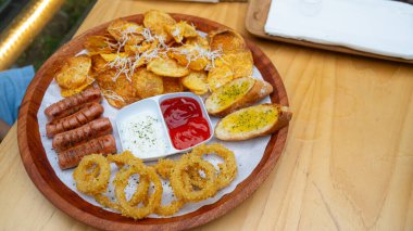 Kızarmış patates ve kızarmış soğan halkalarının fotoğrafı, restoranda bir fotoğrafta, kırmızı biber sosuyla servis ediliyor.